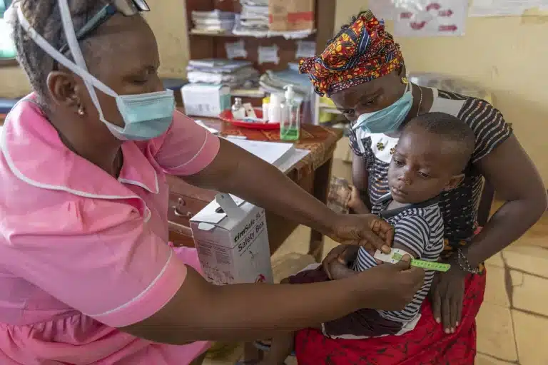 A nurse is measuring a child´s upper arm while he is sitting on his mother's lap.