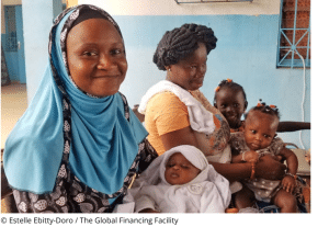 Two mothers and their three children waiting at a health center in Abobo, Côte d'Ivoire. The women who is closetst, smiles at the camera.