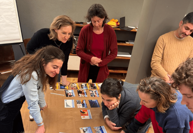 Photo of people gathering around a table, looking at photos on the table and trying to organize the images.