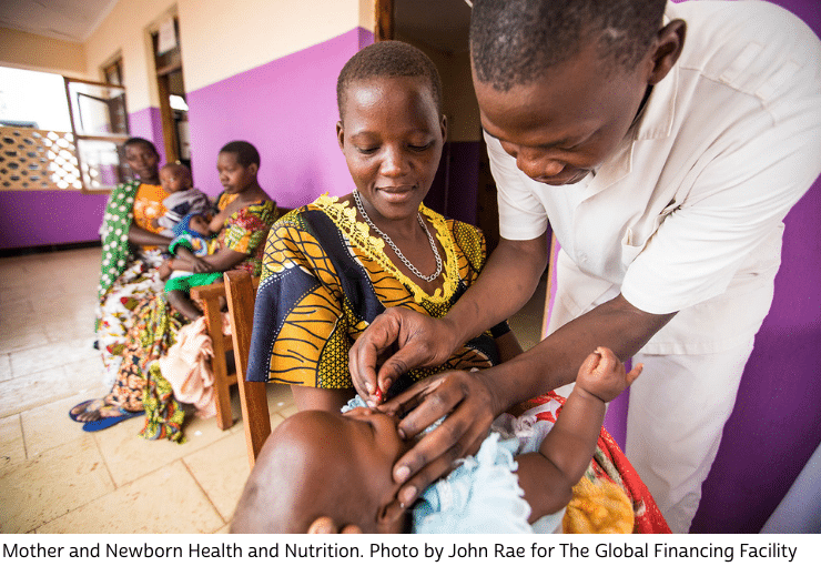 Doctor attending a baby who is laying in the arms of a woman. IN the background more women with children waiting.